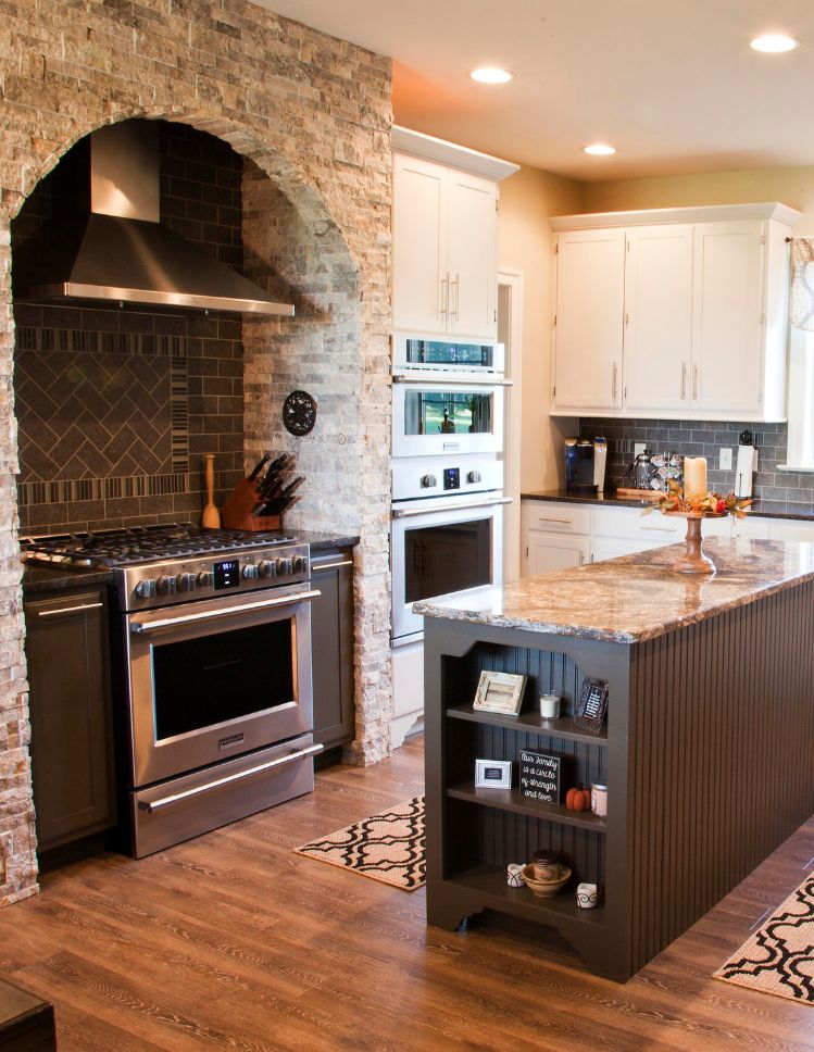 kitchen design with hardwood flooring, white cabinets, and stone accent wall with range hood